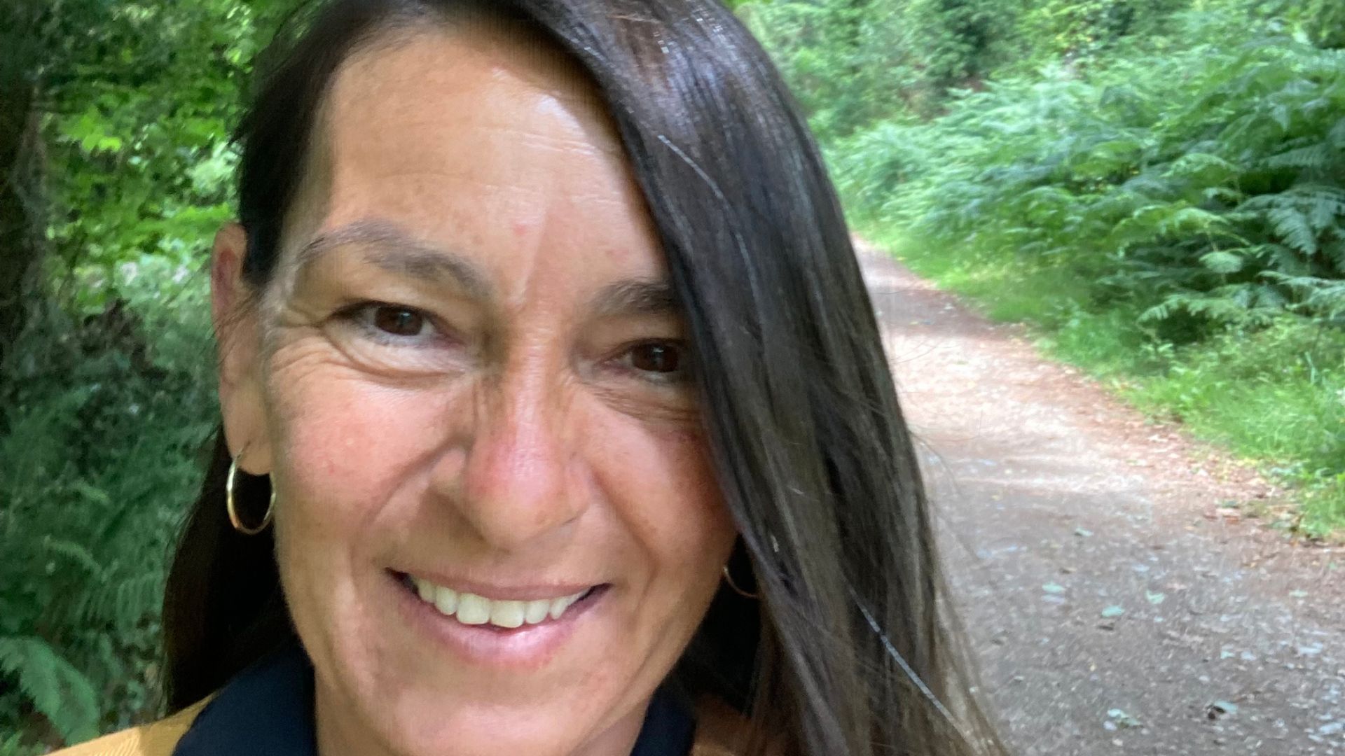 Frau mit langen Haaren steht mit schamanischer Trommel in einem Bach